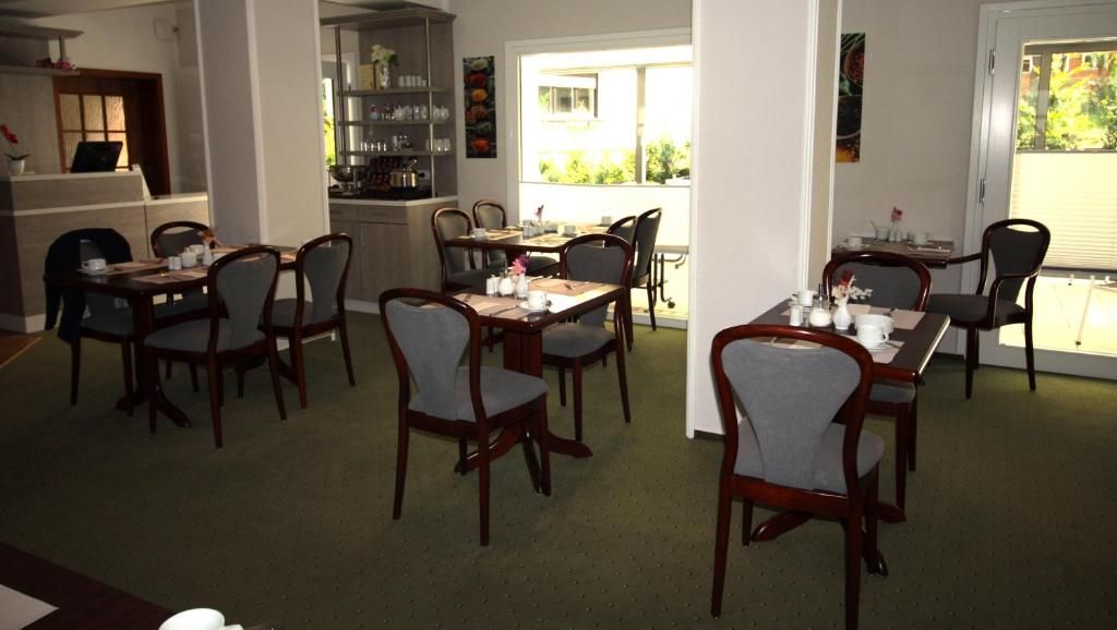 Zona pranzo con diversi tavoli e sedie, una cucina sullo sfondo e vista sull'esterno.
