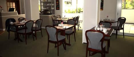 Un comedor con varias mesas y sillas, una cocina al fondo y vistas al exterior.
