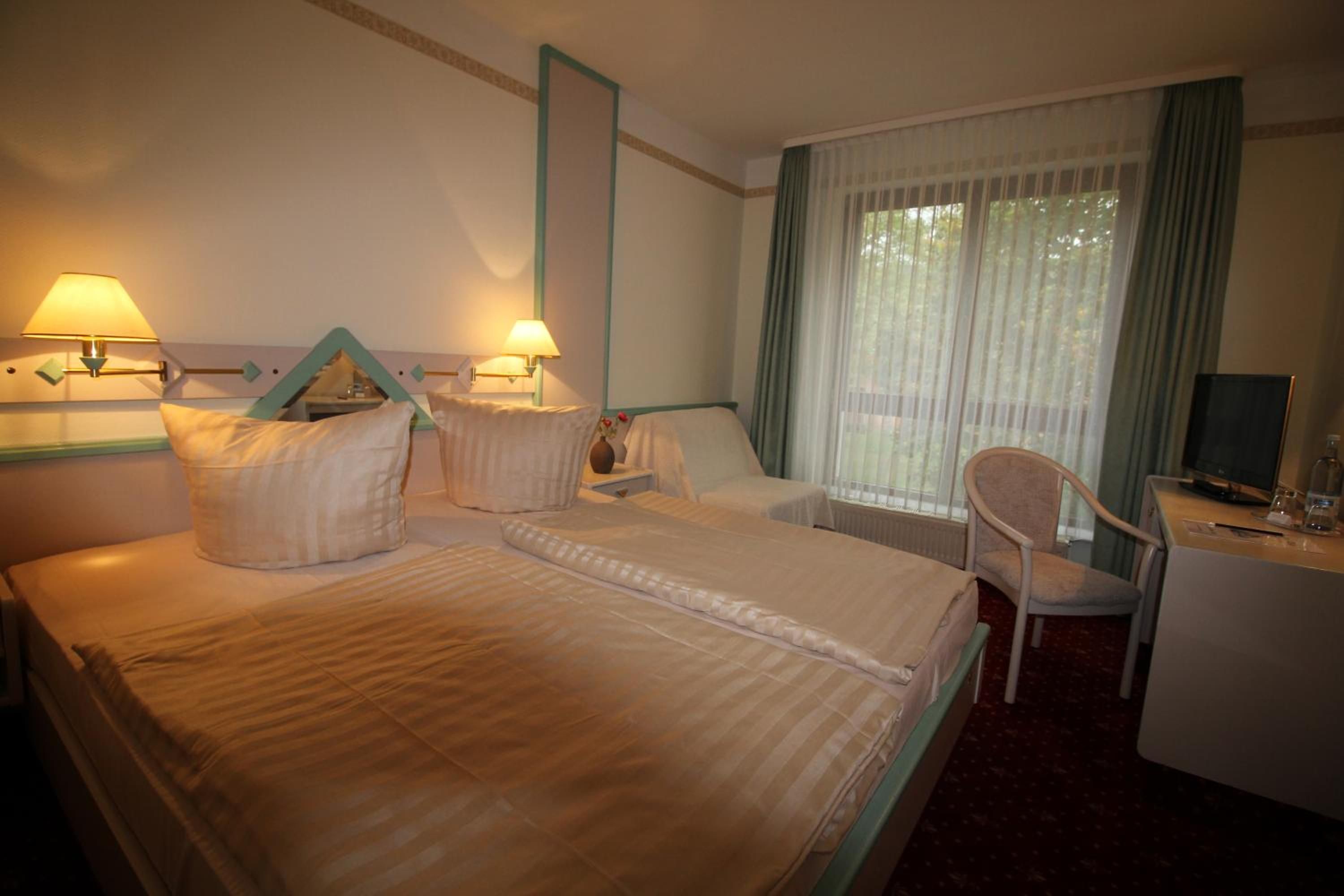A hotel room with two beds, a desk with a chair, a television, and a window with curtains.