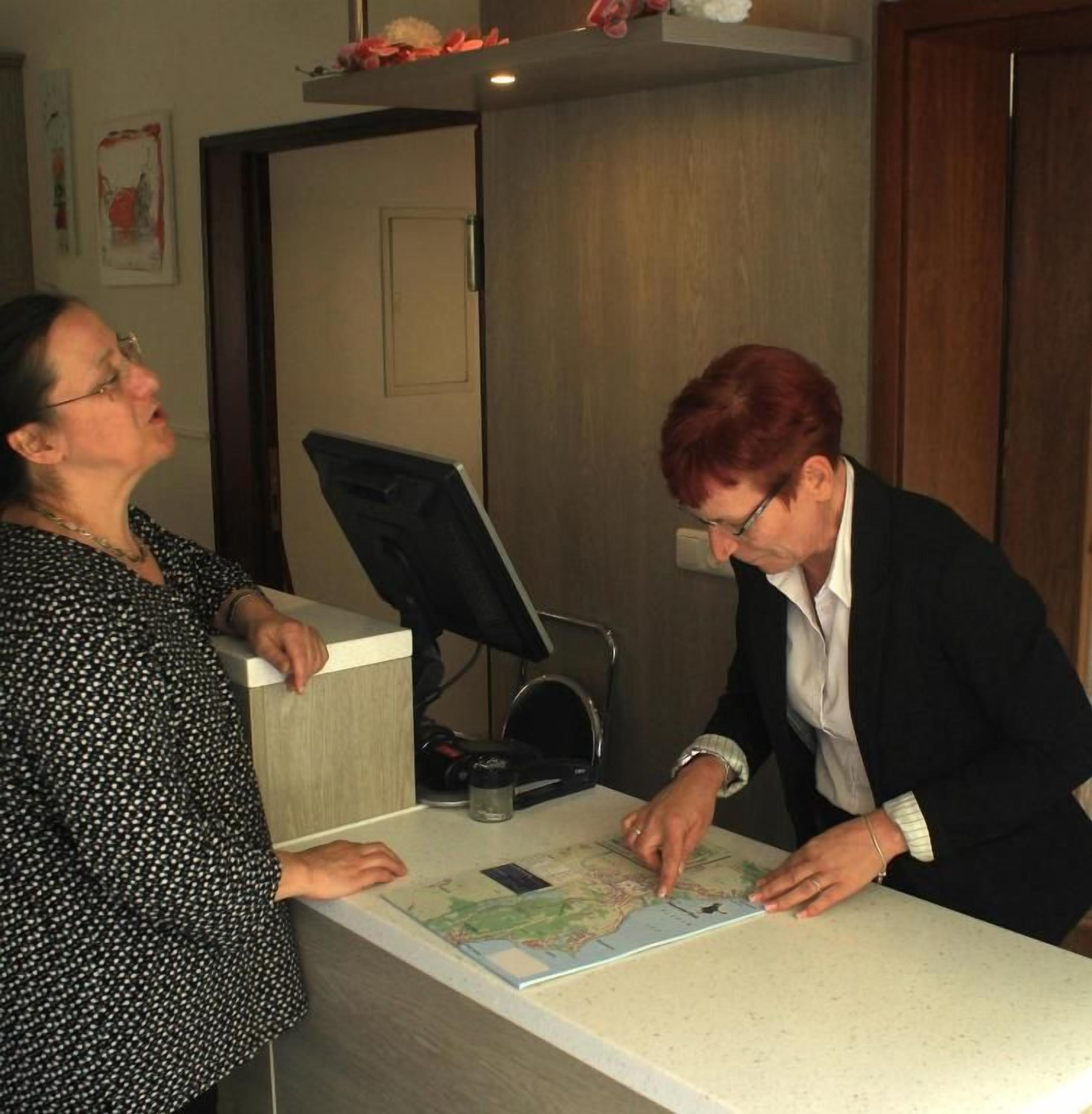 Two people at a reception desk with a map, a computer monitor, and a telephone.