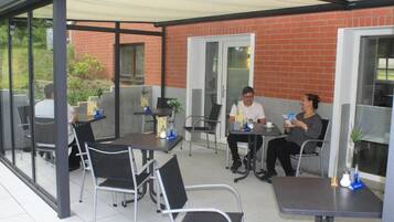 Un área de patio al aire libre con mesas y sillas, una pared de ladrillo y un puerta de vidrio.