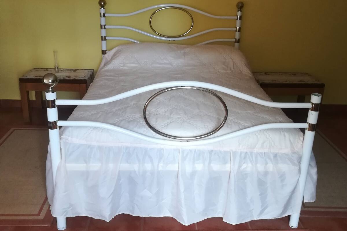 A bed with a white metal frame and a circular headboard, set against a yellow wall with two wall sconces.