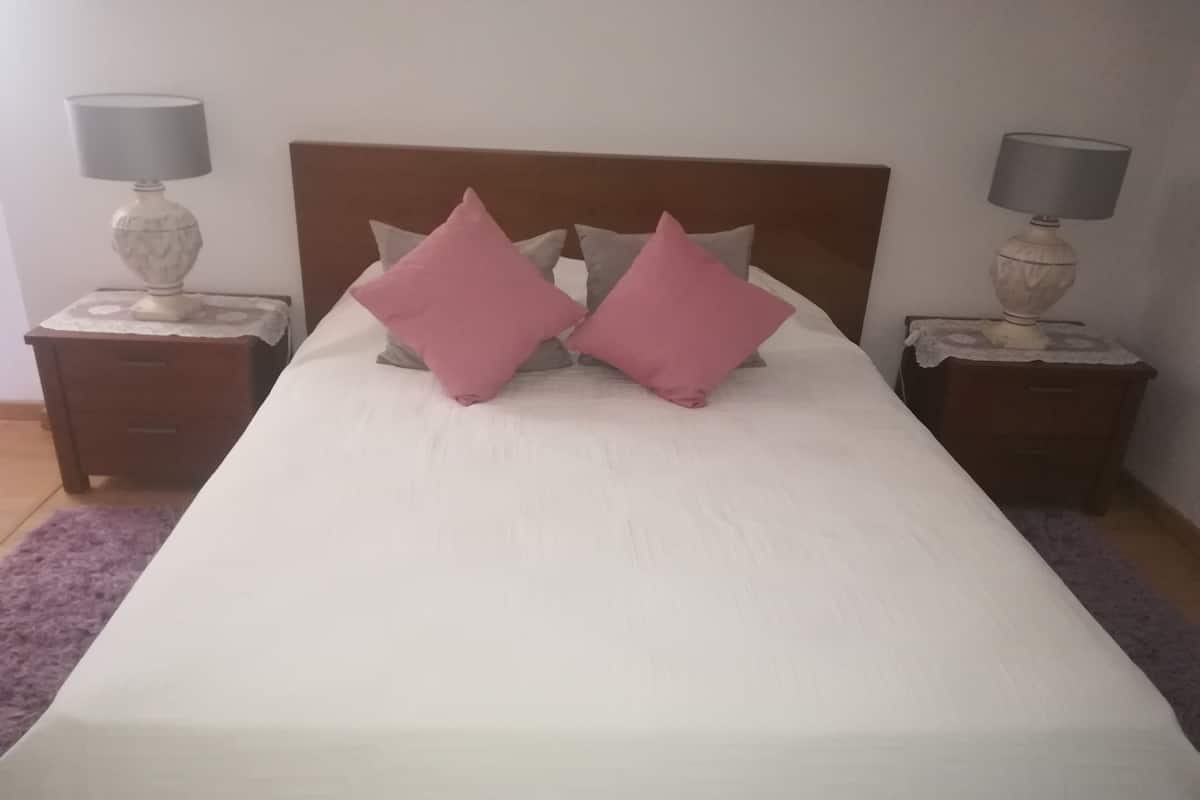 A neatly made bed with a white bedspread and two pink pillows, flanked by two nightstands with lamps and a wooden headboard.
