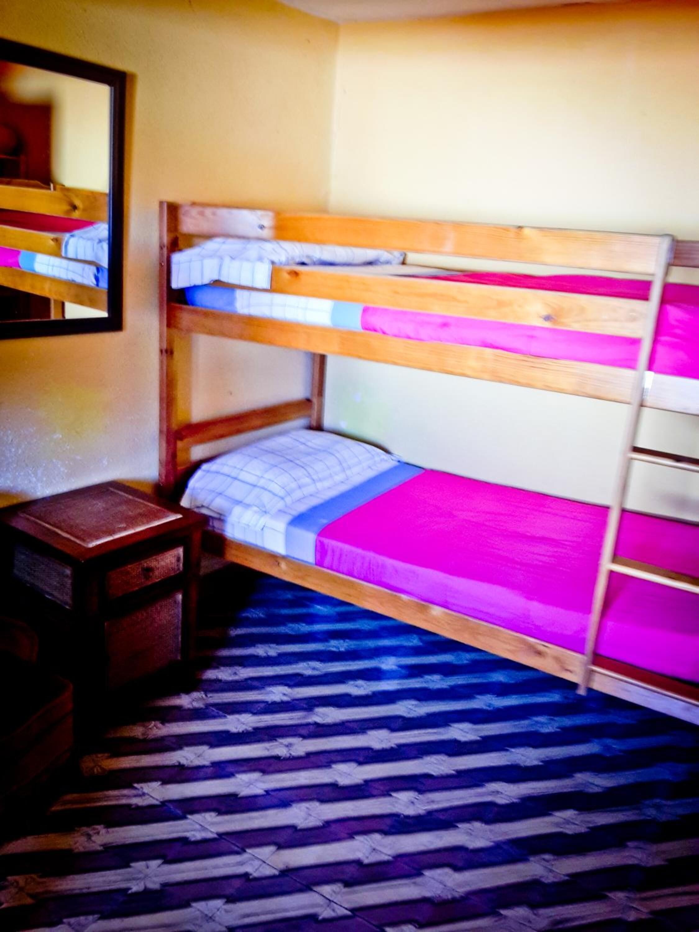 Una cama nido con estructura de madera, una mesita de noche pequeña y una alfombra estampada en el suelo.