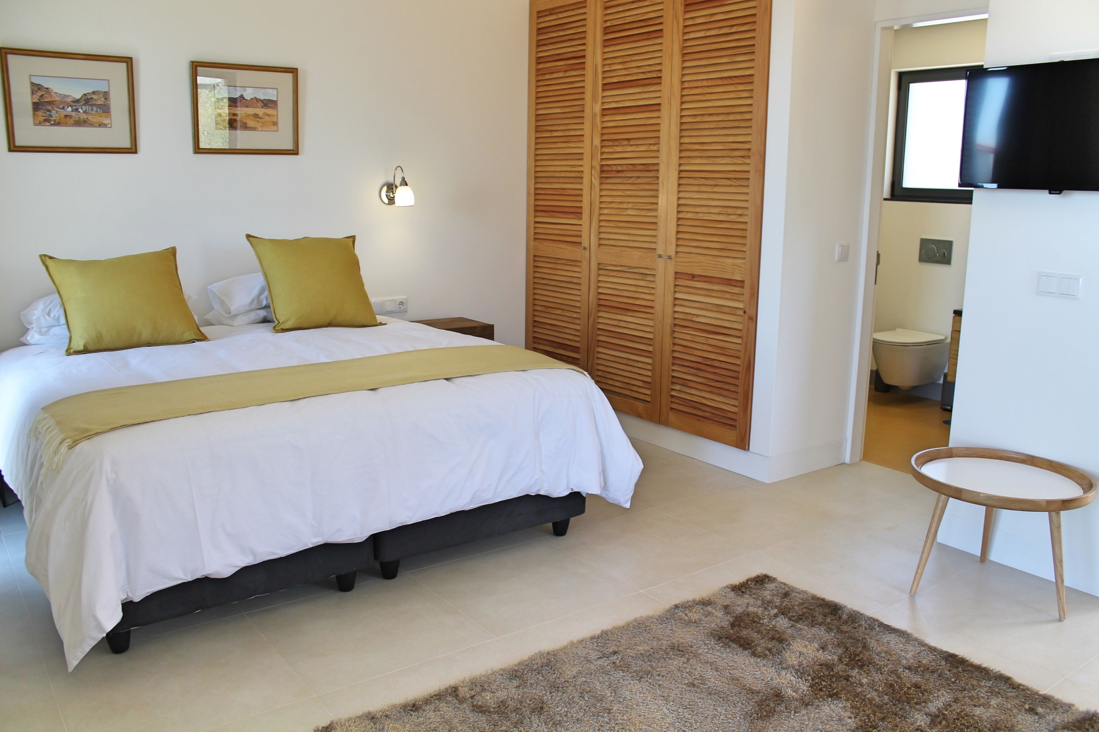 A bedroom with a bed, a wooden wardrobe, a television, and a small table.