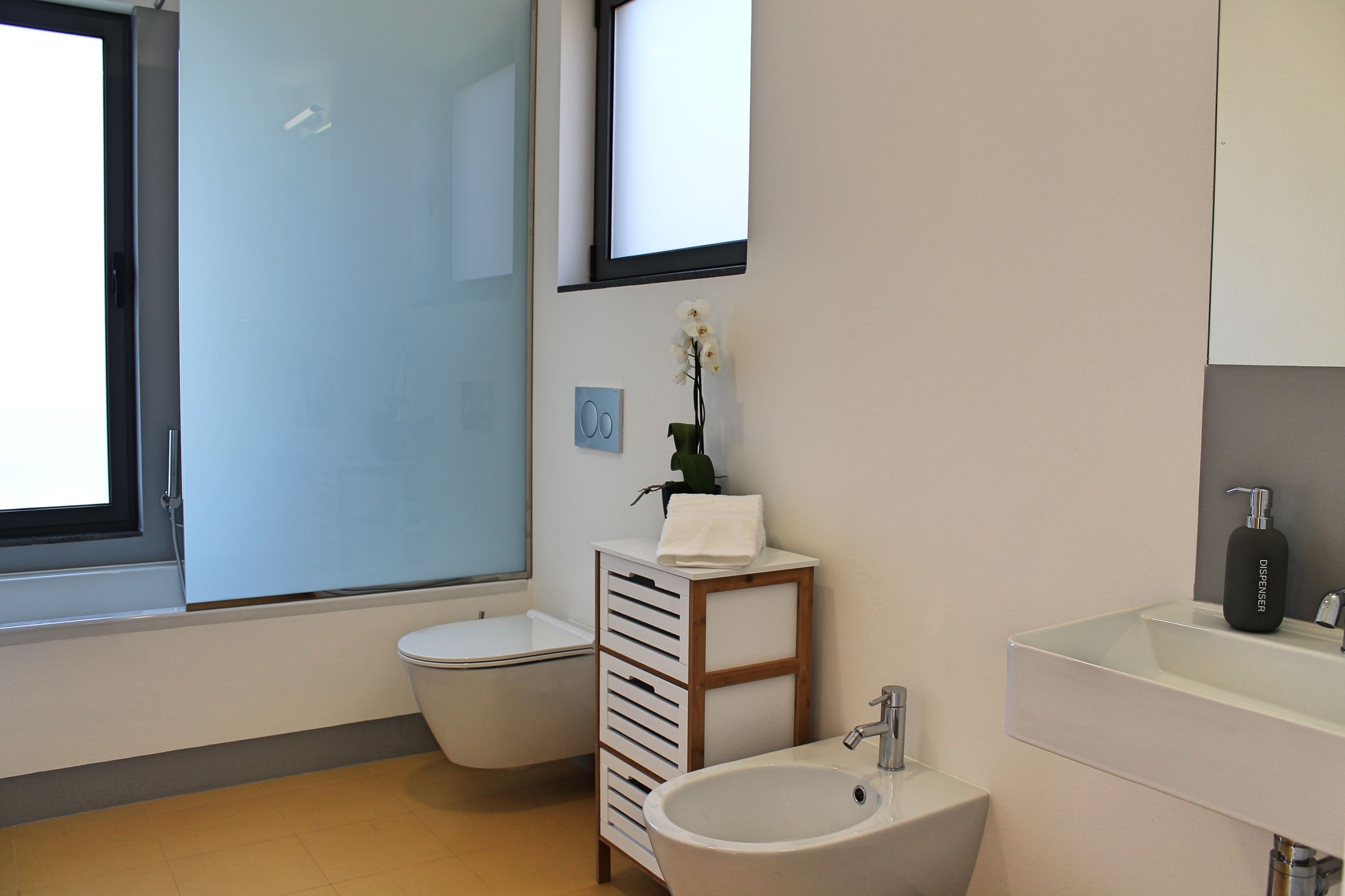A modern bathroom with a toilet, sink, and a small cabinet with a plant.