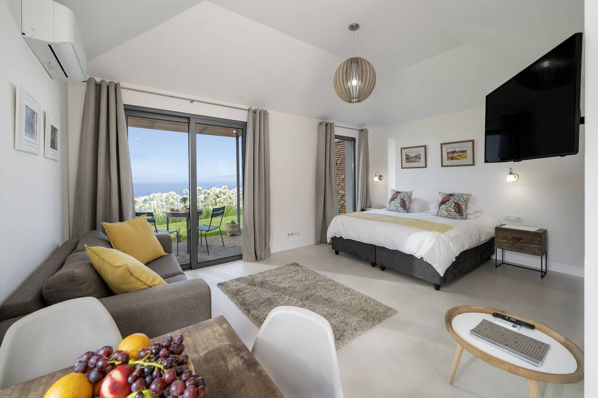 A modern bedroom with a bed, a sofa, a dining table with fruit, and a TV.