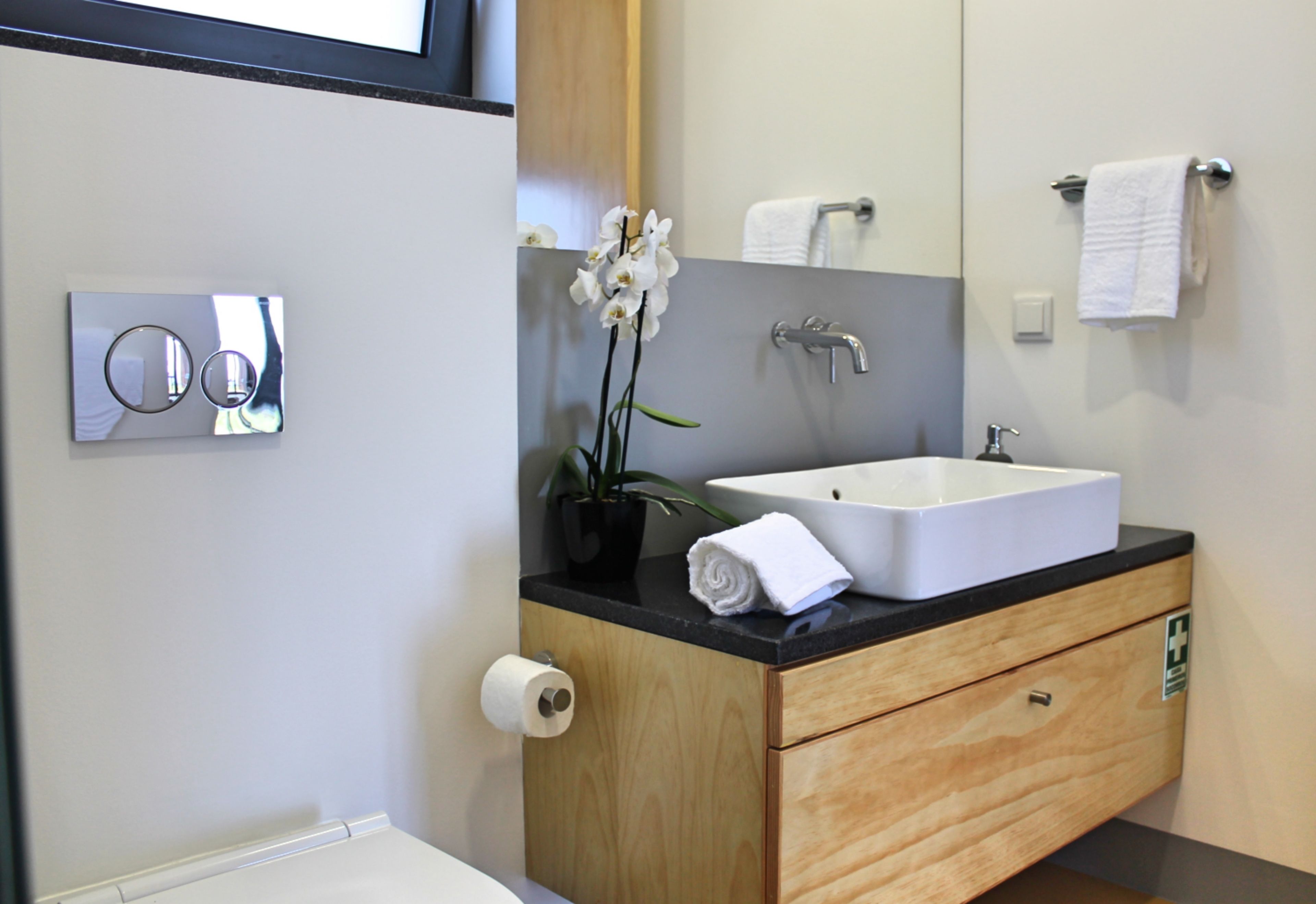 Une salle de bain moderne avec un lavabo blanc, un meuble-lavabo en bois, un miroir, un porte-serviettes et une orchidée en pot.
