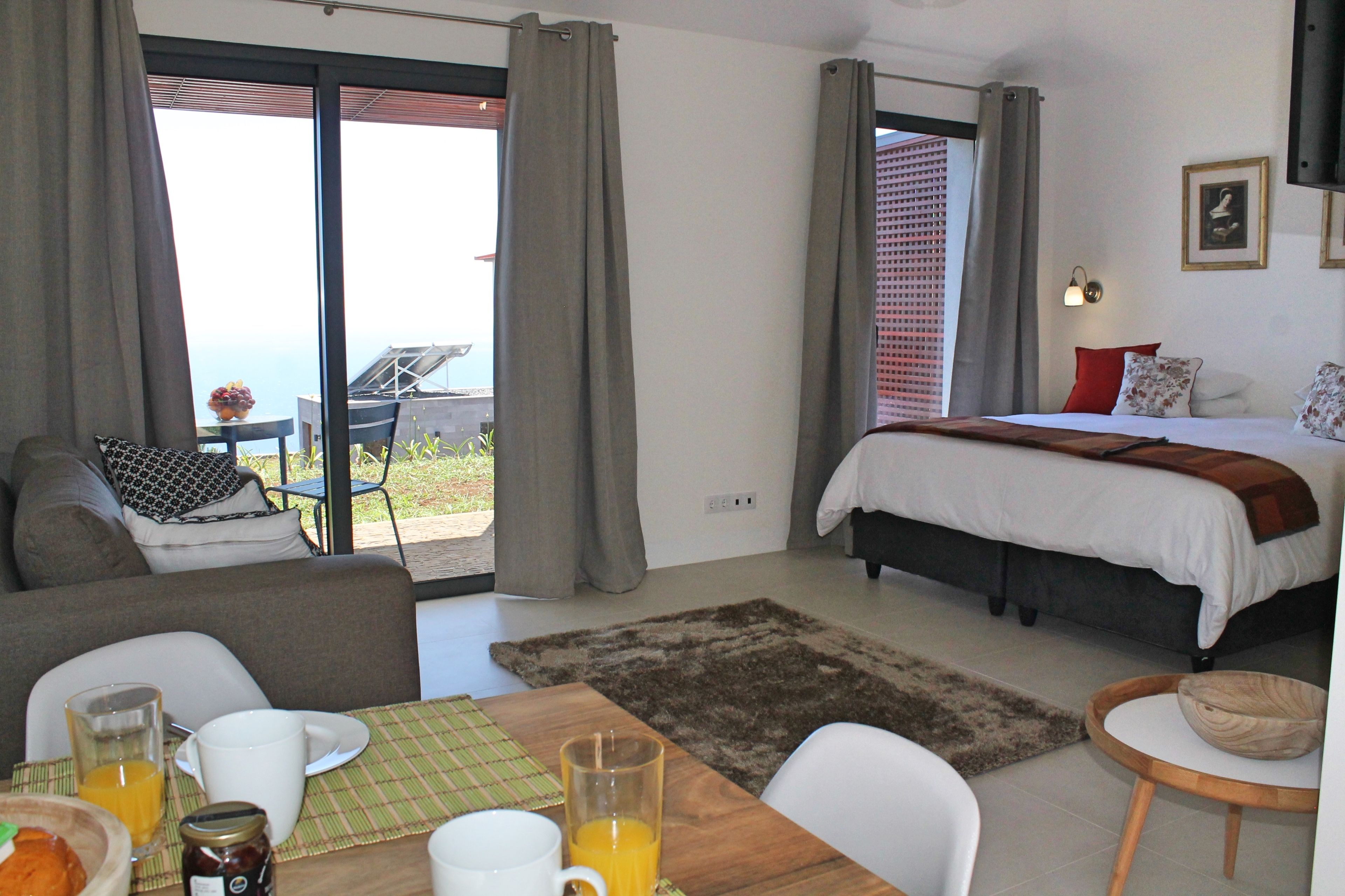 Een hotelkamer met een bed, een slaapbank, een eettafel met ontbijtartikelen en uitzicht op het landschap.