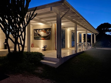 A modern building with a covered patio area, a large painting on the wall, and a fire extinguisher on the ground.