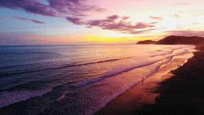 A beach with a sunset, waves, and a distant landform. - Costa Linda Condo 1.3 (Jacó)