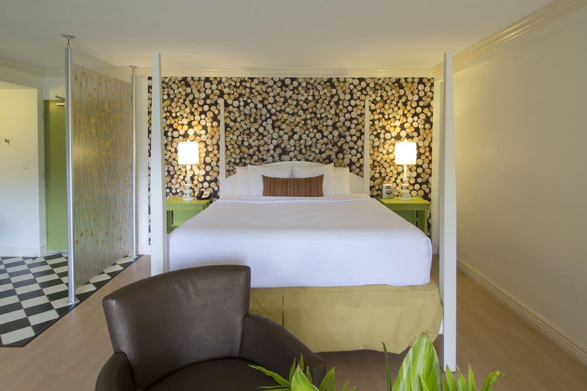 A hotel room with a large bed, two bedside tables with lamps, a chair, and a checkered floor.