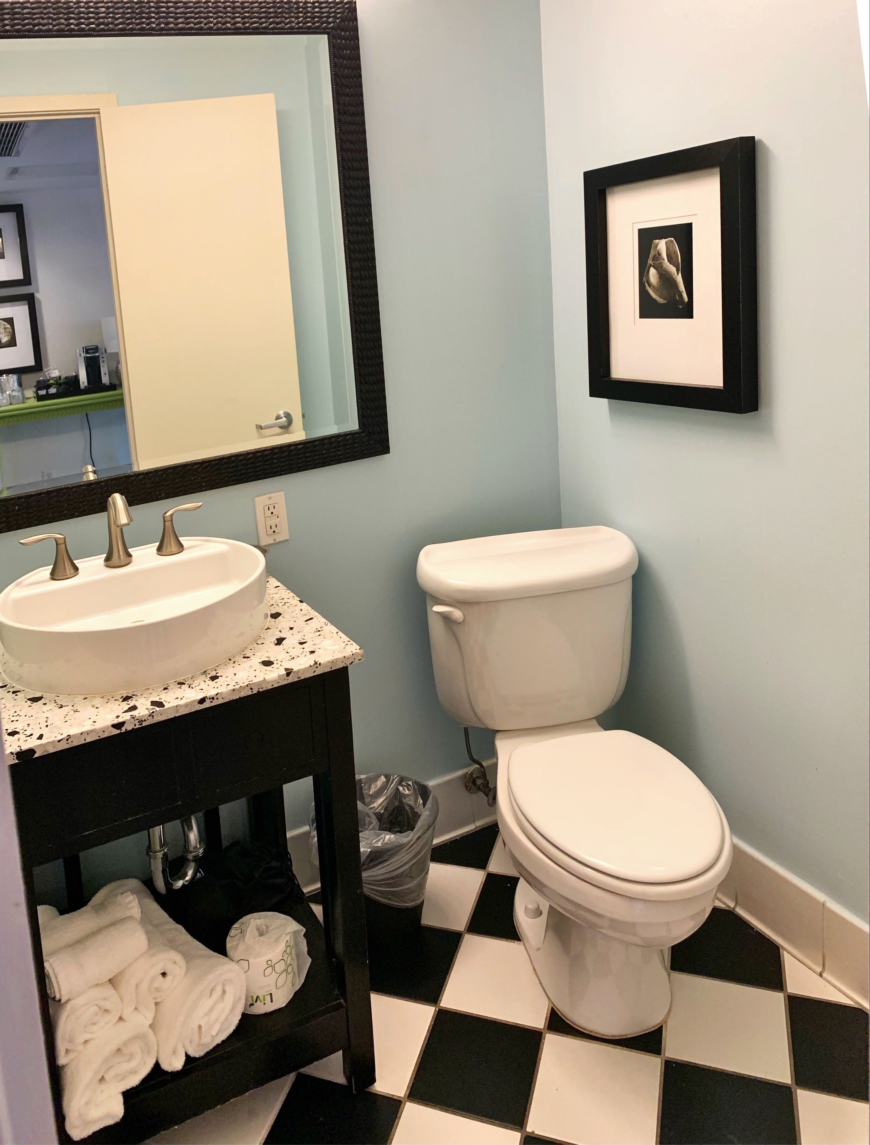 A bathroom with a white sink, a toilet, a framed picture on the wall, and a checkered floor.