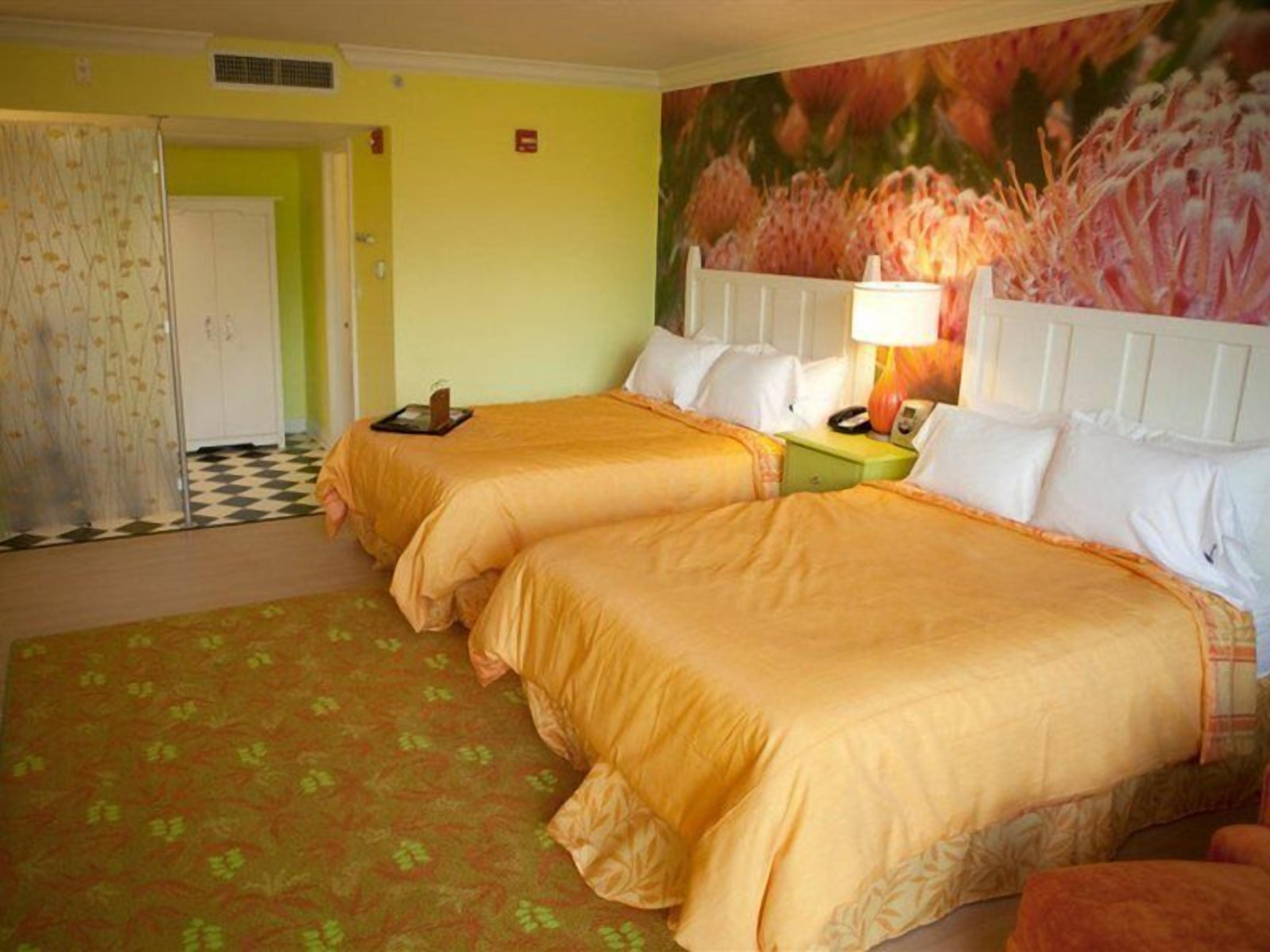 A hotel room with two beds, a checkered floor, a floral wall mural, and a green carpet.