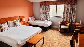Een hotelkamer met twee bedden, een houten hoofdeinde, een bankje, een stoel, een tafeltje en een raam met geruit gordijn.