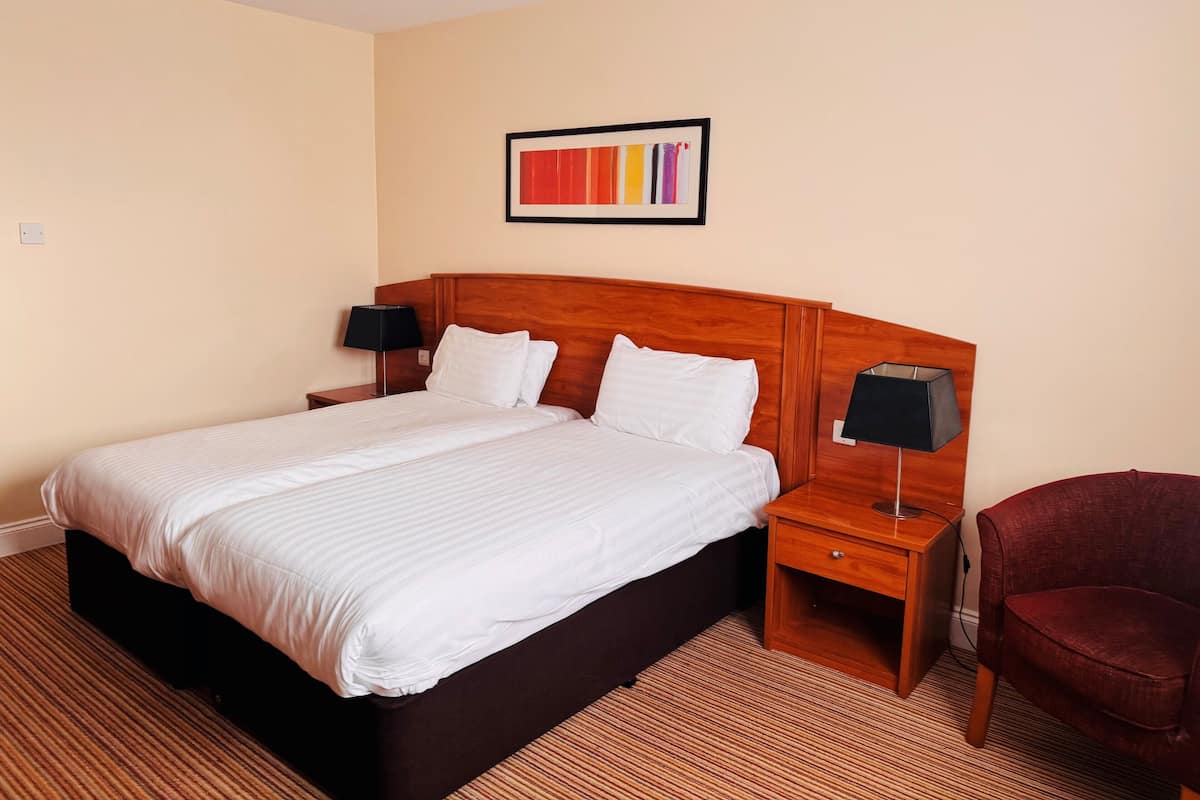 A hotel room with a large bed, two bedside tables with lamps, a red chair, and a colorful abstract painting on the wall.
