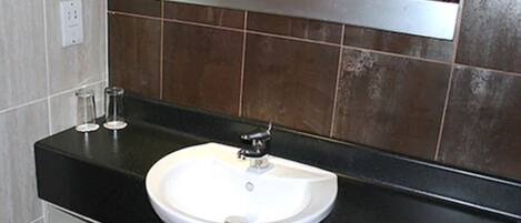 Un baño con lavamanos blanco, encimera negra y un espejo encima.