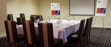 A conference room with a white table, brown chairs, and a projector screen.