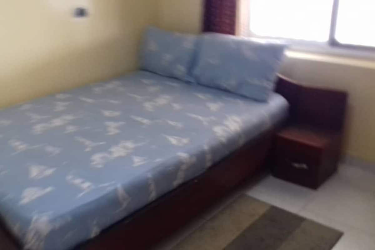Une petite chambre avec un lit simple, une couverture à motifs, une table de chevet et une fenêtre avec des rideaux.
