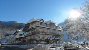 Ein traditionelles Chalet-Gebäude mit mehreren Etagen, einem markanten Balkon und einem Schild, das es als Hotel kennzeichnet.