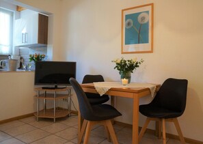 Un petit coin repas équipé d’un téléviseur, de deux chaises, d’une table et d’un vase avec des fleurs.