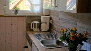 Eine Küche mit Holzbalken, einem Fenster mit Vorhängen, einer Kaffeemaschine, einem Spülbecken und einer Vase mit Blumen.