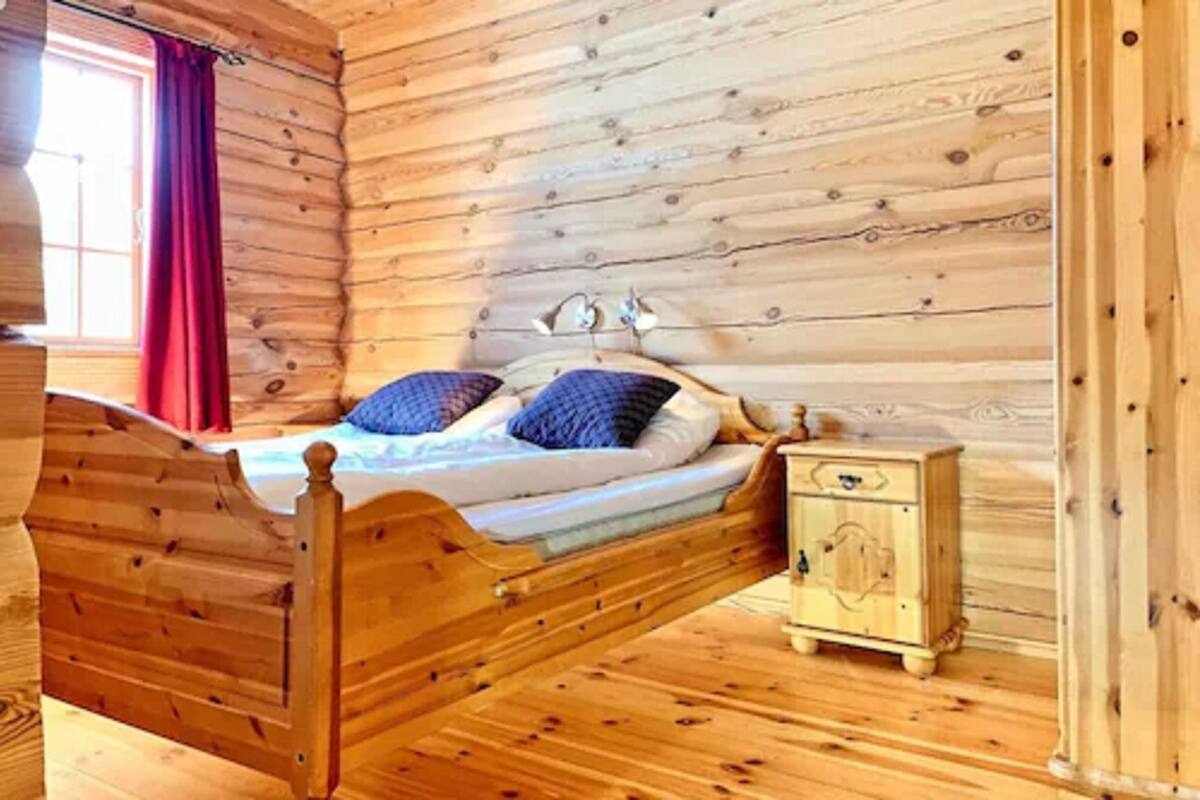 Dormitorio de cabaña de madera con una cama, una mesita de noche y una ventana con cortinas rojas.