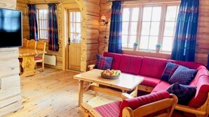 A cozy cabin interior with a wooden dining table, a sofa, and a television. - Savalen Fjellhotell & Spa (Tynset)