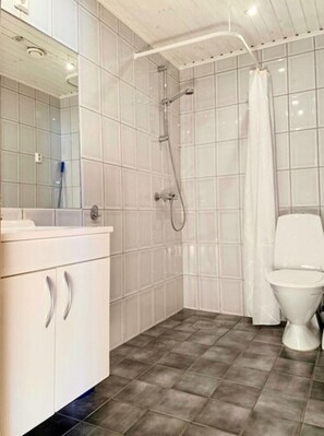 Features a white tiled shower area, toilet, and vanity with mirror and sink.