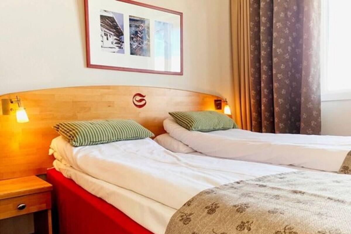 Habitación de hotel con dos camas, cabecera de madera, colcha roja y un cuadro enmarcado en la pared.