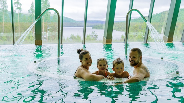 A family in a large indoor swimming pool with a view of a lake and mountains through large windows. - Savalen Fjellhotell & Spa (Tynset)