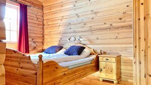 A wooden cabin room with a bed, a nightstand, and a window with red curtains. - Savalen Fjellhotell & Spa (Tynset)