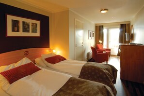 Two single beds with patterned bedspreads and red pillows, a flat-screen TV, and a desk with a chair.