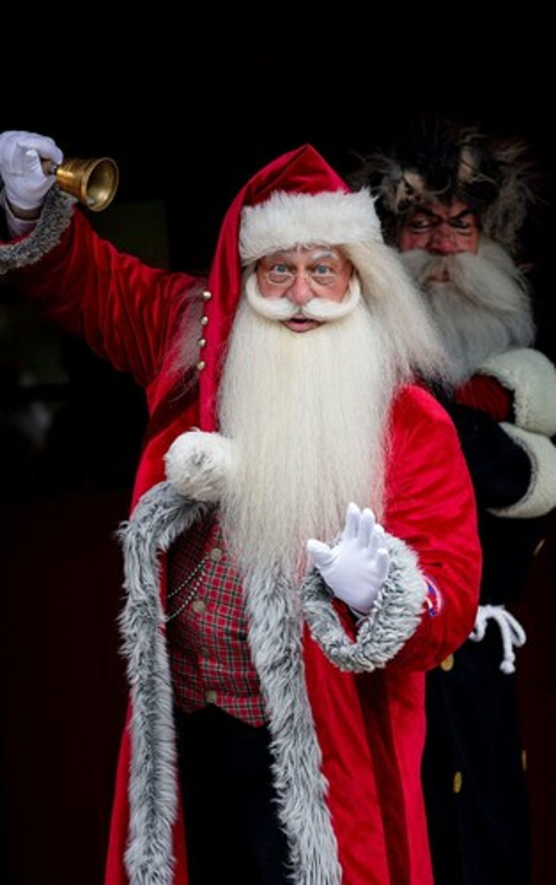 Uma pessoa vestida de Papai Noel segurando um sino.