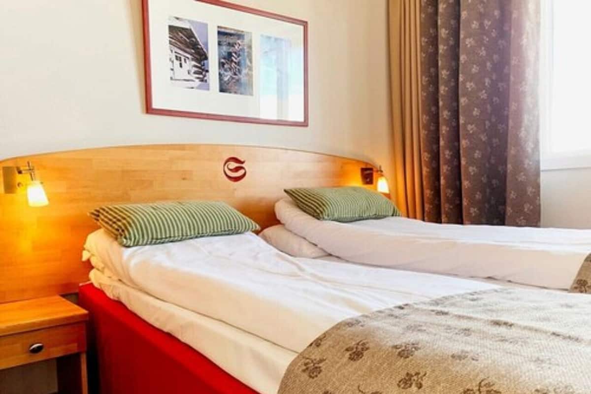 Habitación de hotel con dos camas, cabecera de madera, colcha roja y un cuadro en la pared.