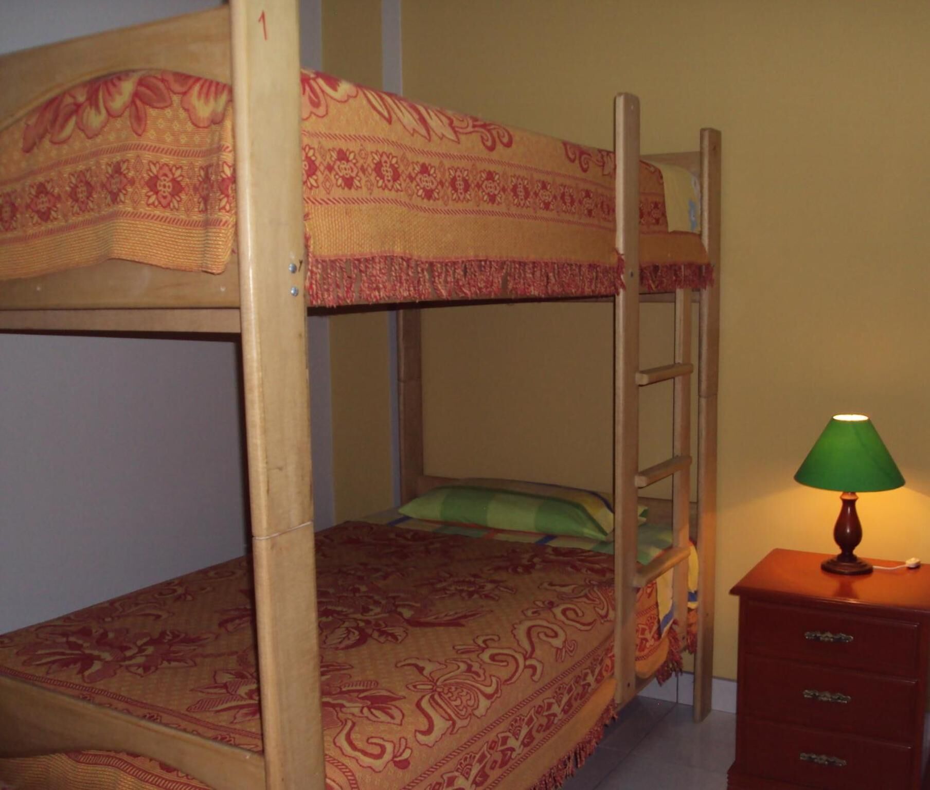 Una cama litera con un edredón estampado, una escalera y un aparador con una lámpara.