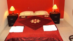 A hotel room with a red wall, a bed with a floral bedspread, two bedside tables with lamps, and a white floor. - Nasca Lodge (Nazca)