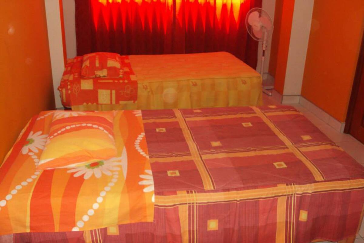 A room with a bed and a small table, both covered with orange and red patterned bedspreads.
