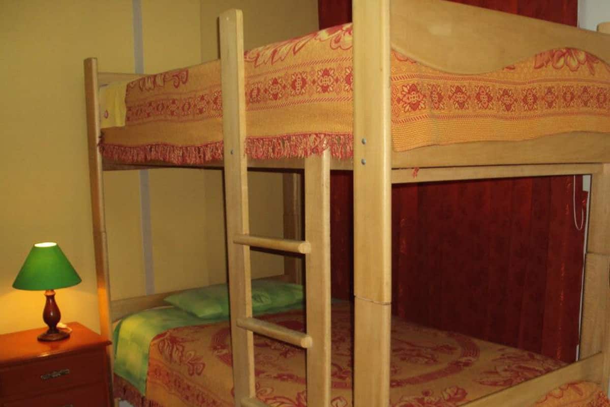 A bunk bed with a ladder, a bedside table with a lamp, and a patterned bedspread.
