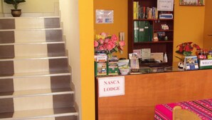 A reception desk with a sign reading "NASCA LODGE," a staircase, and a table with a colorful tablecloth. - Nasca Lodge (Nazca)