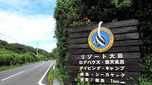 A wooden sign with a logo and Japanese text indicating a location 1 km ahead. - Resort Ohshima (Kushimoto)