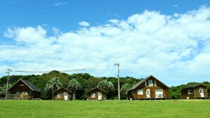 A row of wooden cabins with a grassy field and trees in the background. - Resort Ohshima (Kushimoto)