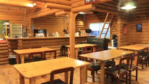 A log cabin interior with wooden tables and chairs, a bar area, and a kitchen visible through an open door. - Resort Ohshima (Kushimoto)