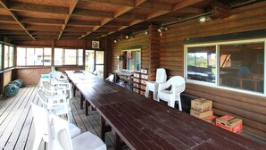 A covered outdoor dining area with wooden tables and white plastic chairs, a wooden ceiling, and large windows. - Resort Ohshima (Kushimoto)