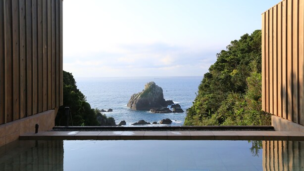 A view from a pool area with a wooden deck, a clear sky, and a rocky island in the distance. - Resort Ohshima (Kushimoto)
