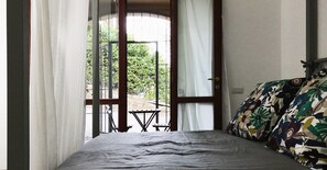 A room with a bed, a window with curtains, and a view of greenery outside. - Agriturismo Castagna Amara (Montevecchia)