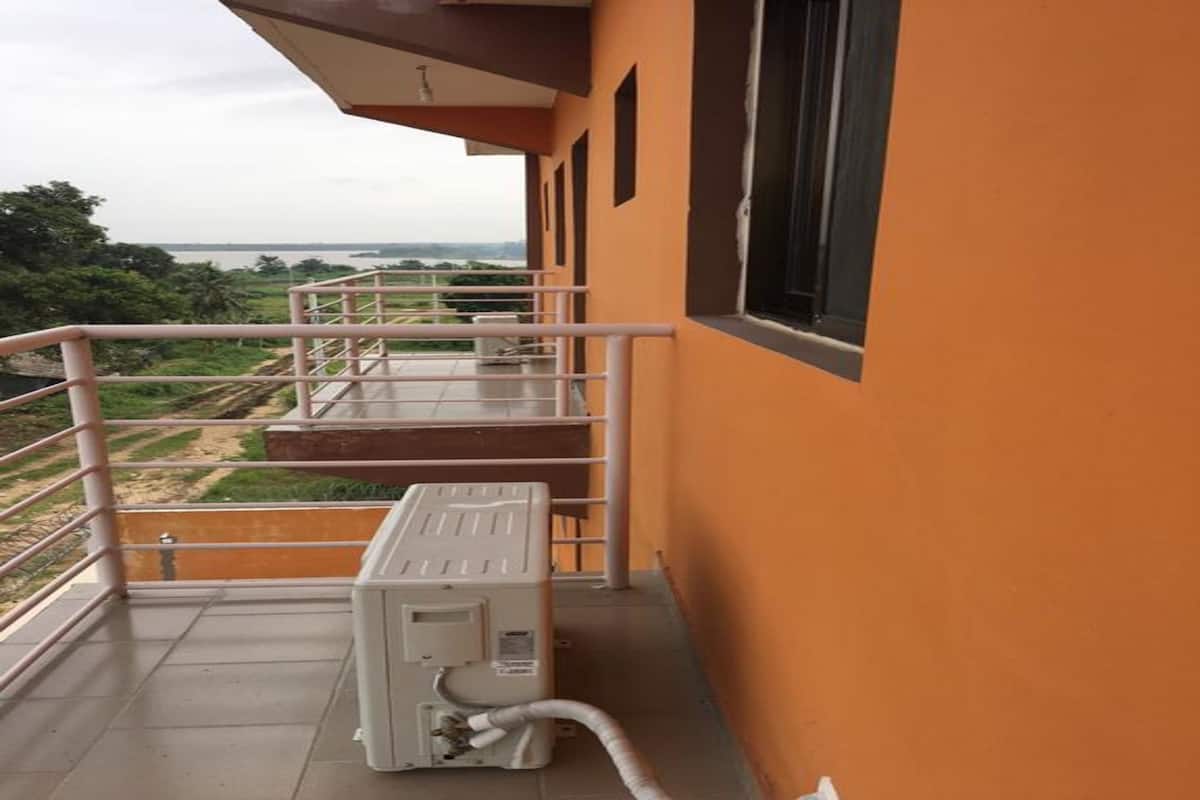 A balcony with a view of a river and greenery, a white air conditioning unit, and a metal railing.