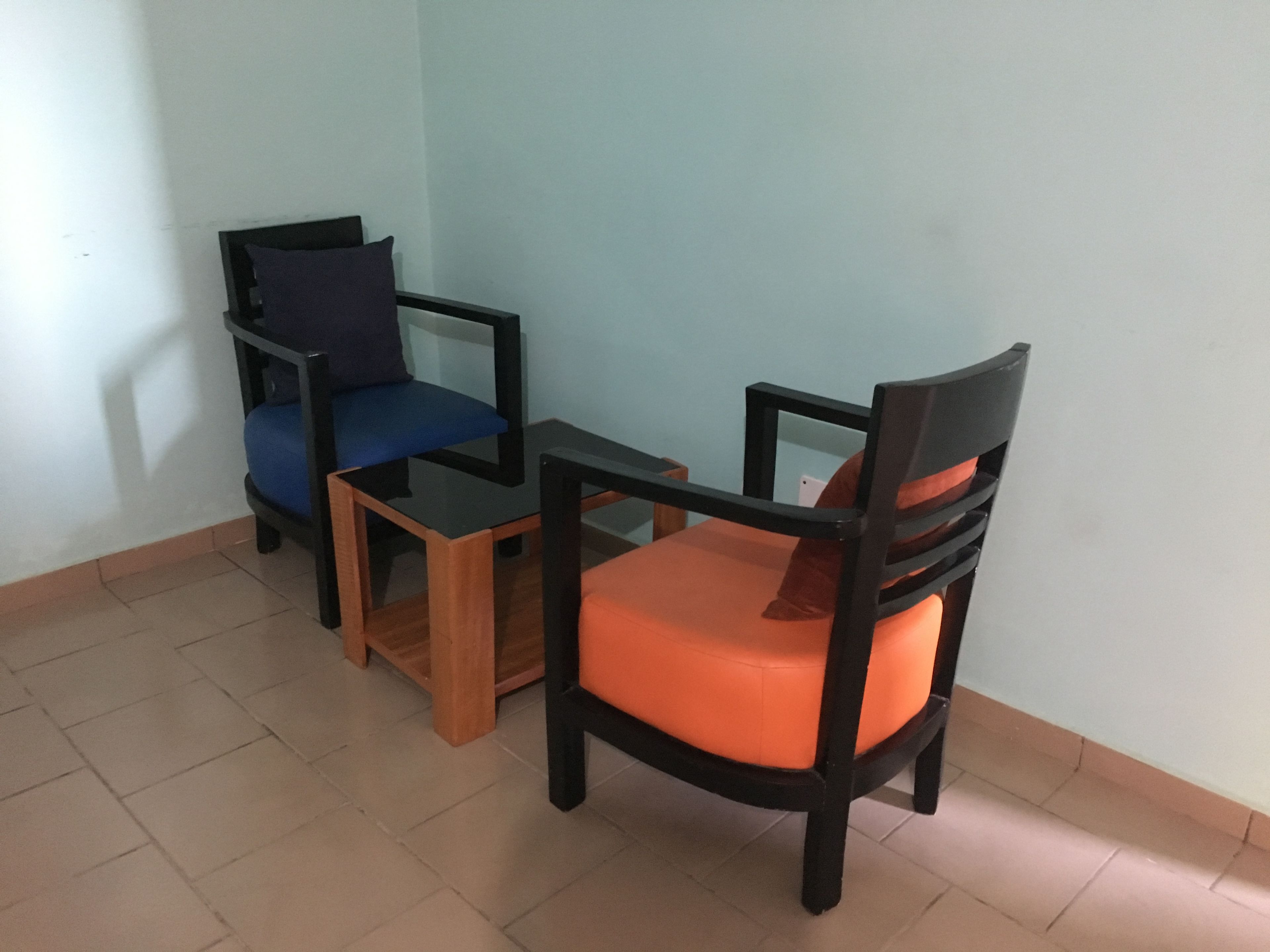 Une pièce comprenant deux chaises en bois avec des coussins, l’une bleue et l’autre orange, et une petite table noire.