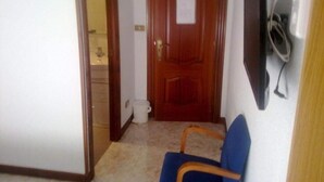 Un pasillo con una puerta de madera, un sillón azul y un aire acondicionado de pared.