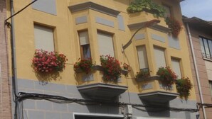 Un edificio con varias ventanas, algunas con contraventanas, y balcones adornados con macetas de flores.